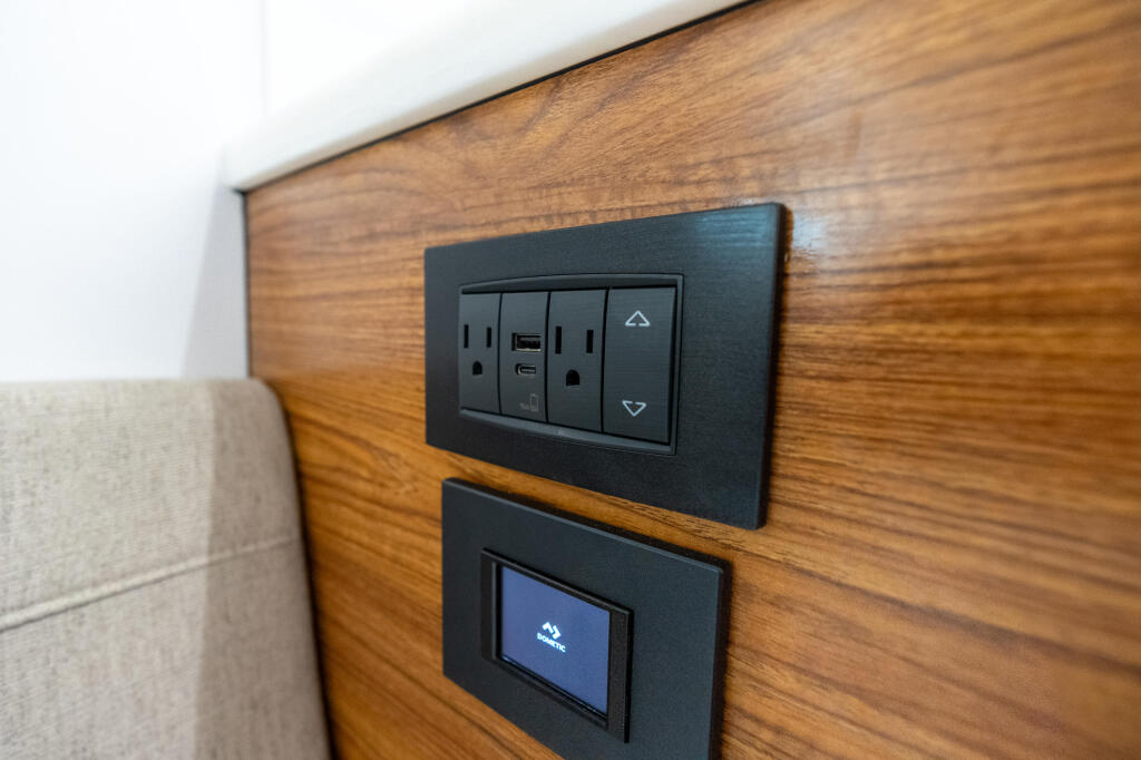 Marine cabin wall with wooden paneling featuring black electrical outlets, USB port, and control screen for onboard systems