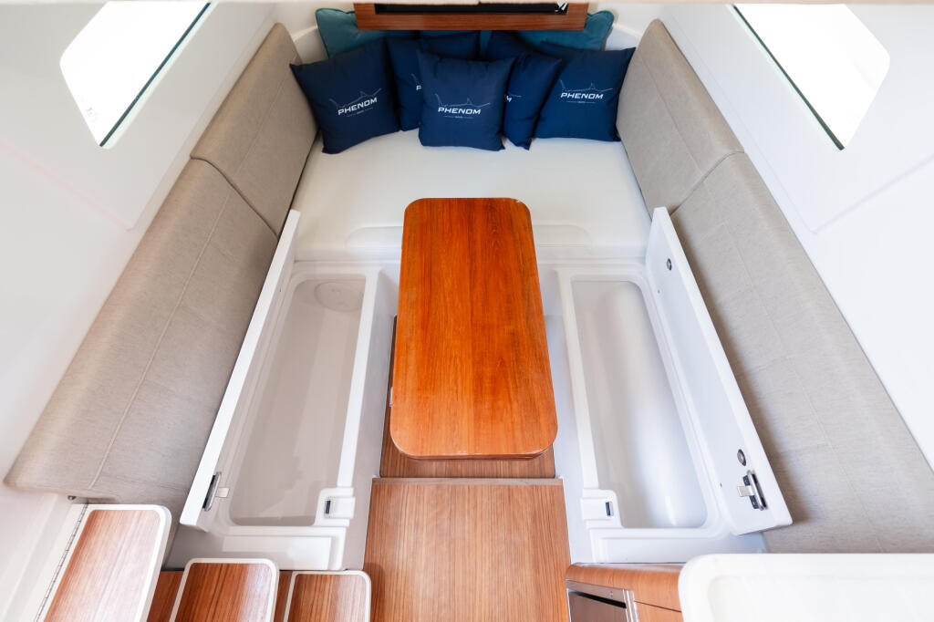 Overhead view of a boat cabin with beige seating, navy pillows, wooden table, and storage compartments