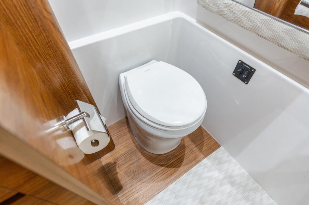 Modern marine head with white porcelain toilet, wood trim, and control panel in compact cabin space