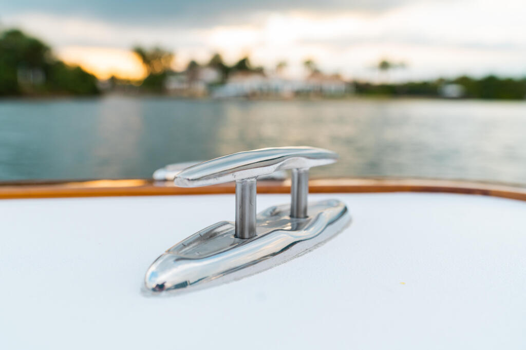 Close-up of polished chrome cleat hardware on a boat deck with waterfront marina in the background