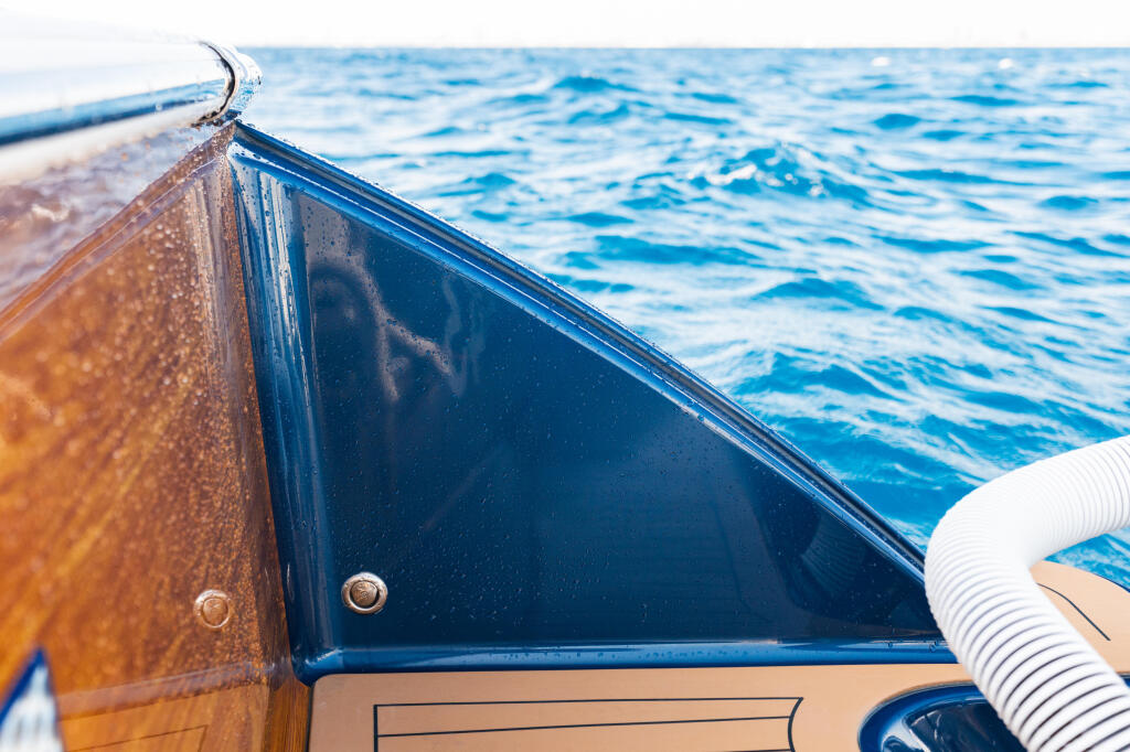Close-up of boat's tumblehome design showing curved hull and open window with blue water beyond