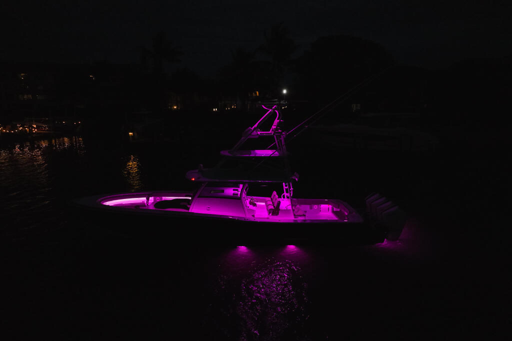 Fishing boat illuminated with vibrant magenta underwater lights and deck lighting at night