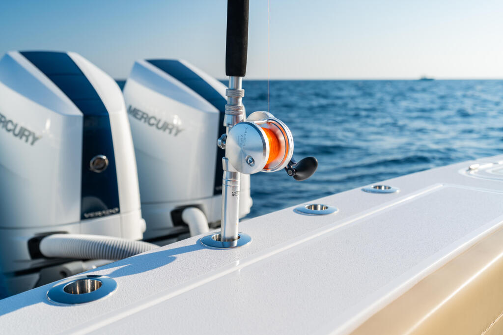 Fishing rod with orange reel mounted in a screwless rod holder on a boat gunwale with Mercury engines visible