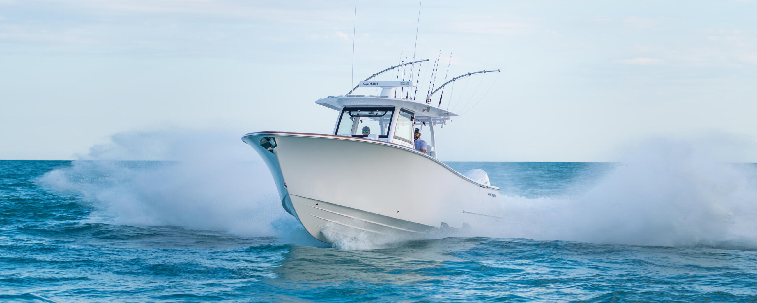 White center console fishing boat running at speed through ocean waves with fishing rod holders on the hard-top