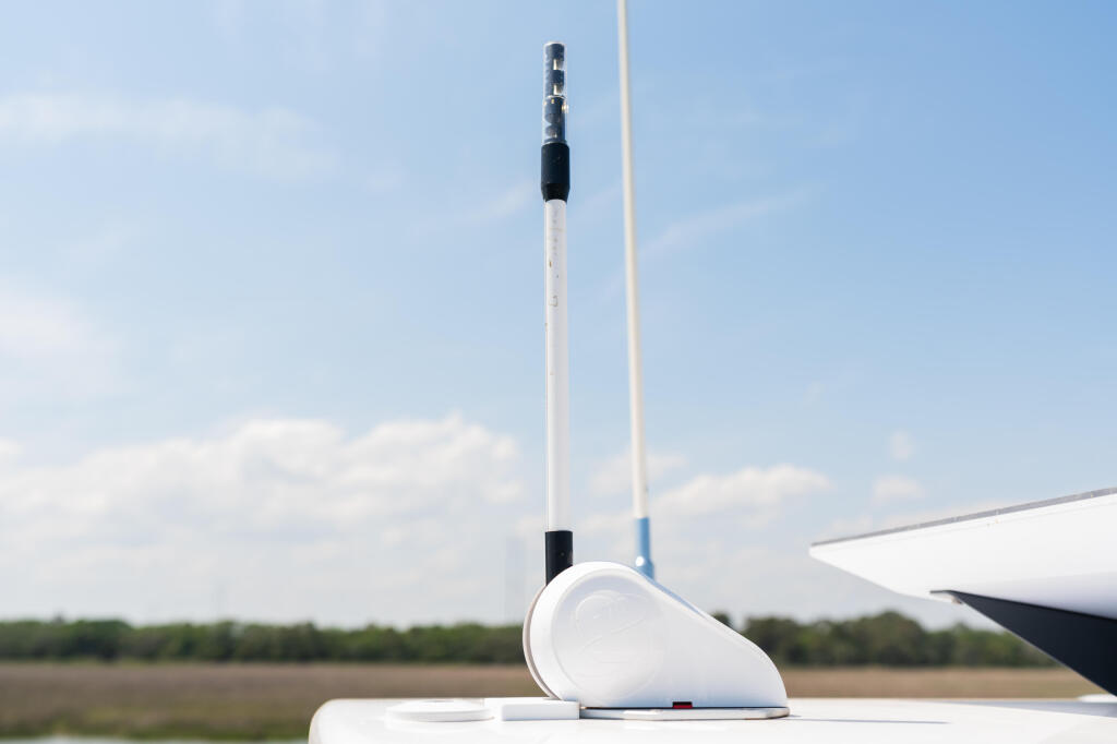 Boat's white antenna and GPS dome mounted on hardtop against blue sky and waterway