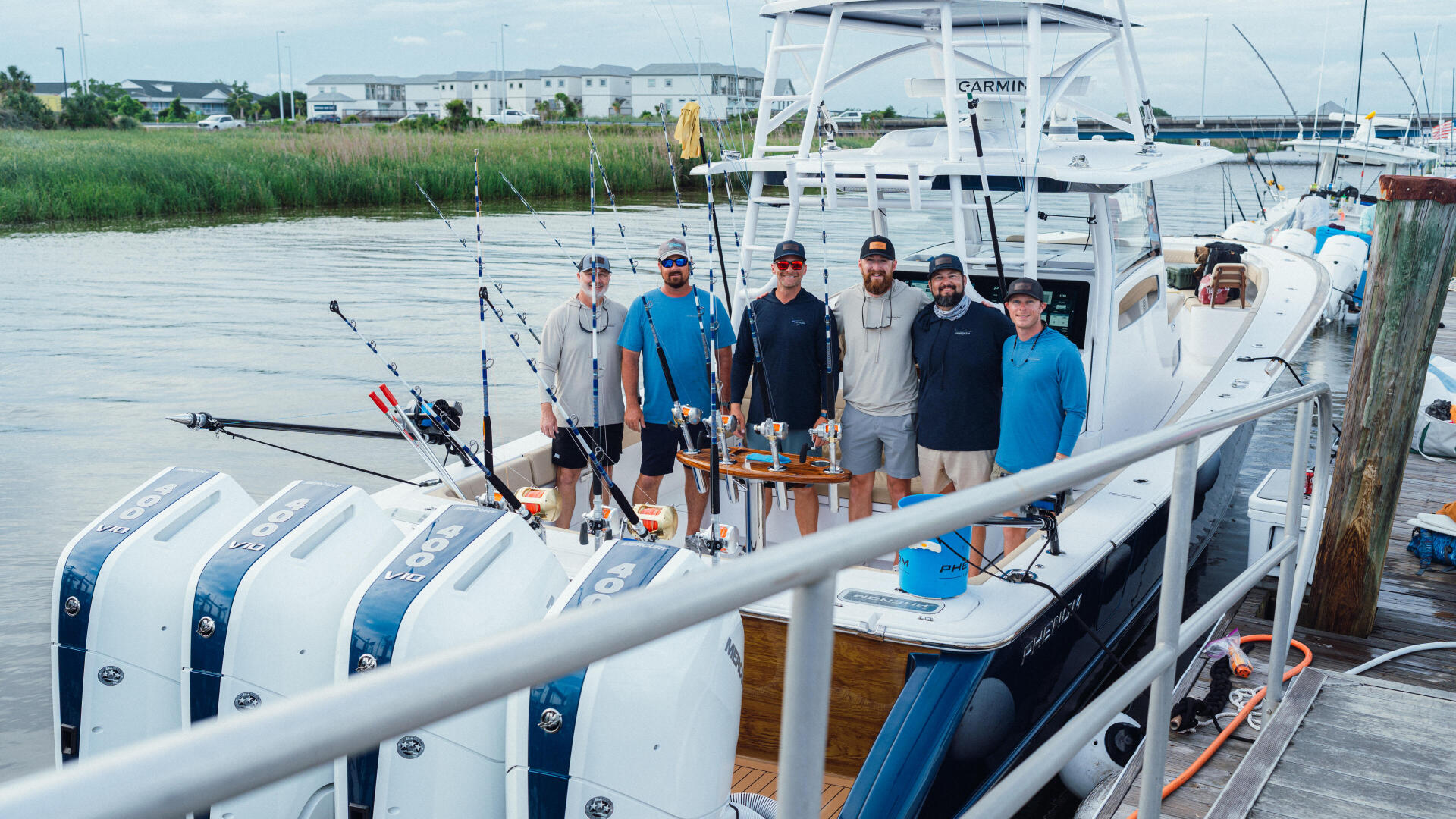 Group of anglers posing on fishing boat docked at marina with multiple fishing rods rigged and ready