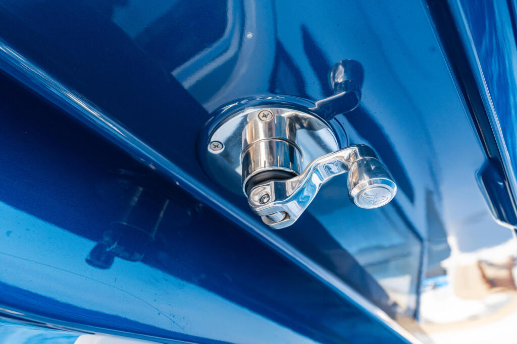 Polished chrome fishing reel mounted on a blue boat rail against bright sunlight