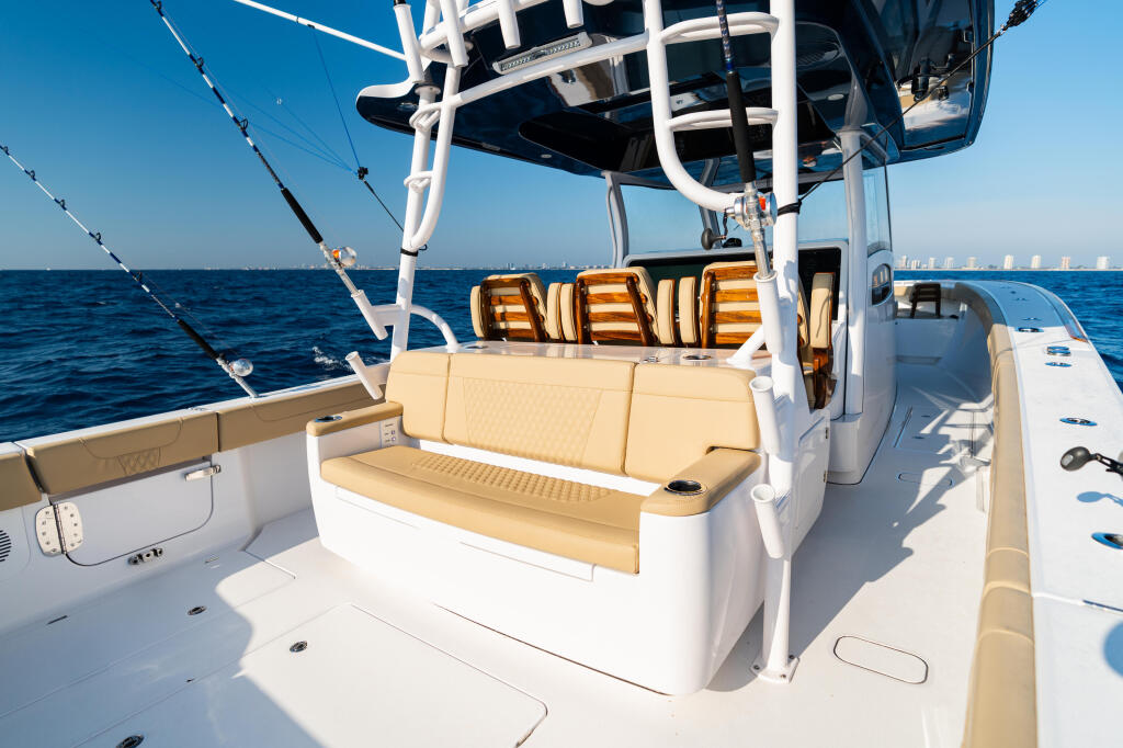 Sportfishing boat's aft cockpit with tan seating, rod holders, and hard-top canopy overlooking calm blue ocean