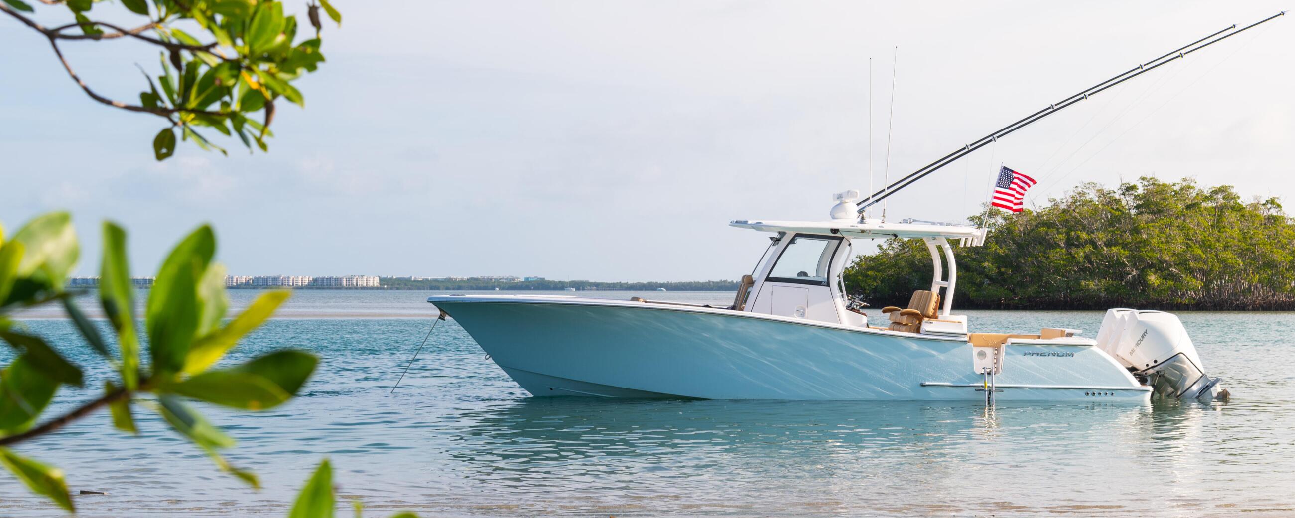 Blue and white center console boat anchored in shallow turquoise water near a sandy beach with mangroves