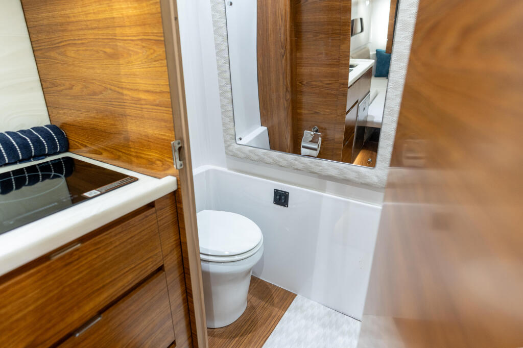 Boat cabin bathroom with white toilet, sink vanity, mirror, and warm wood cabinetry throughout