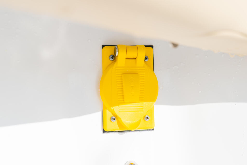 Bright yellow electrical outlet receptacle mounted on white boat surface