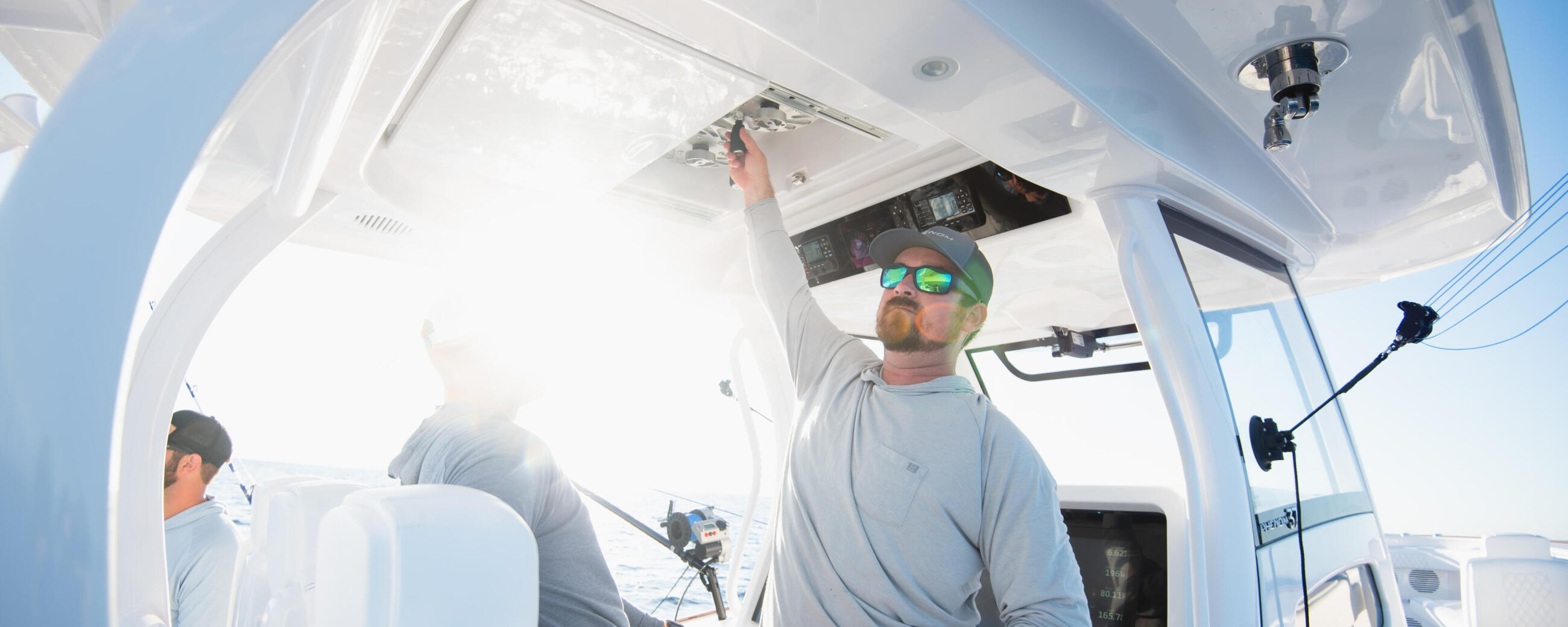 Anglers inside a center console boat's cabin with hard-top, one holding a fishing rod while looking upward at interior features