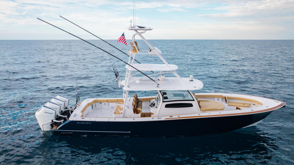 White and navy sport fishing yacht anchored offshore with twin outboard engines and extended fishing outriggers