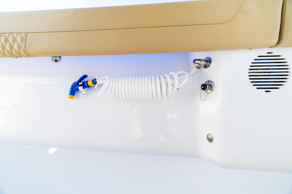 Overhead view of boat cabin showing coiled freshwater hose with blue connector, electronics speaker, and deck hardware